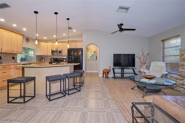 kitchen featuring a kitchen bar, tasteful backsplash, black appliances, light brown cabinets, and ceiling fan