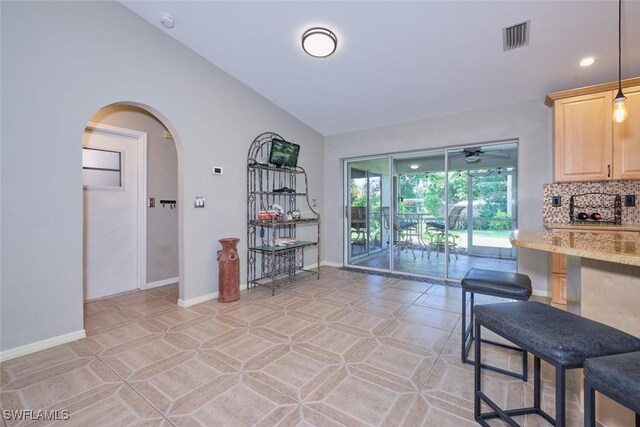 interior space with ceiling fan, light brown cabinetry, light stone countertops, vaulted ceiling, and light tile patterned floors