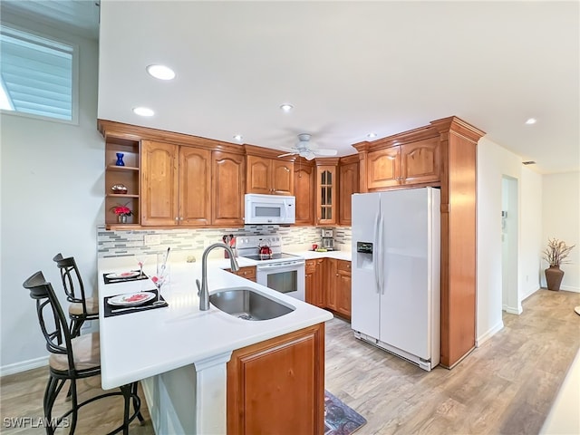 kitchen featuring white appliances, sink, a kitchen breakfast bar, kitchen peninsula, and light hardwood / wood-style flooring