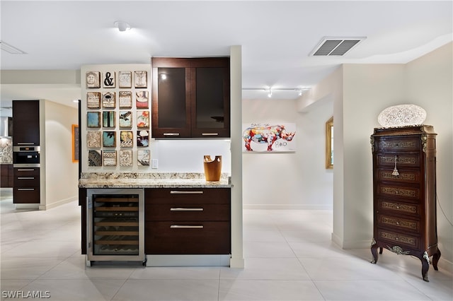 bar with dark brown cabinets, light stone counters, and wine cooler