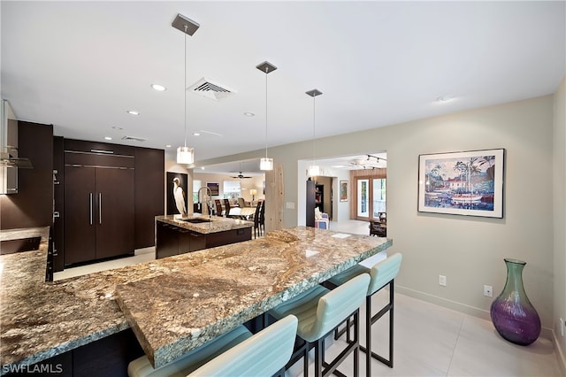 kitchen with ceiling fan, sink, an island with sink, pendant lighting, and dark brown cabinets