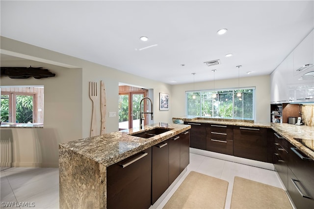 kitchen with a center island with sink, hanging light fixtures, a healthy amount of sunlight, and sink