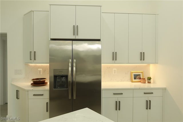 kitchen with white cabinetry, stainless steel fridge, decorative backsplash, and light stone countertops