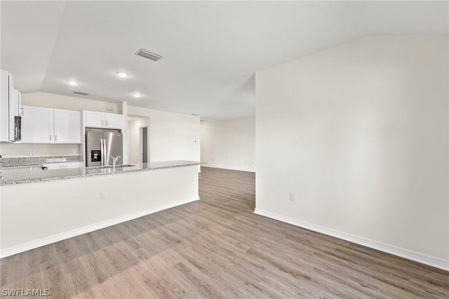 kitchen featuring vaulted ceiling, light wood-type flooring, white cabinets, stainless steel fridge, and light stone counters