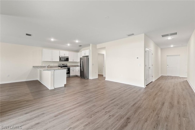 kitchen with light hardwood / wood-style floors, kitchen peninsula, white cabinetry, appliances with stainless steel finishes, and light stone counters