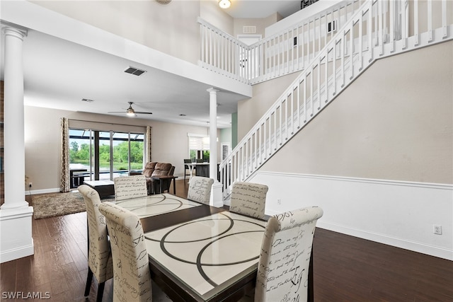 dining space with dark hardwood / wood-style floors, ceiling fan, ornate columns, and a towering ceiling