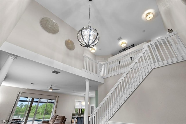 staircase featuring ceiling fan with notable chandelier, decorative columns, and a high ceiling