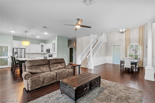 living room featuring ornate columns, sink, ceiling fan with notable chandelier, and wood-type flooring