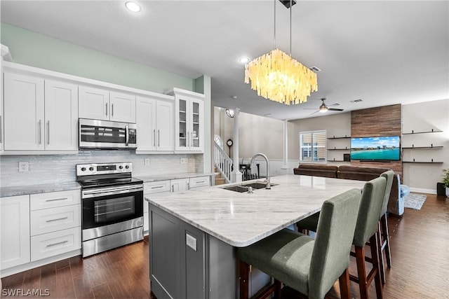 kitchen with decorative light fixtures, appliances with stainless steel finishes, a kitchen breakfast bar, an island with sink, and white cabinets