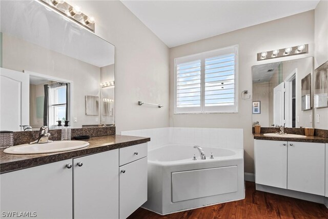 bathroom with vaulted ceiling, hardwood / wood-style flooring, a bath, and double sink vanity