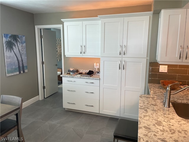 kitchen with white cabinetry, backsplash, light stone counters, dark tile patterned flooring, and sink