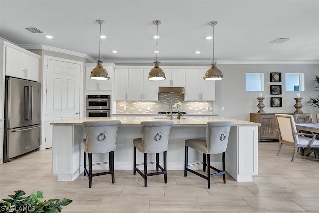 kitchen featuring decorative light fixtures, tasteful backsplash, stainless steel appliances, light stone countertops, and a kitchen island with sink