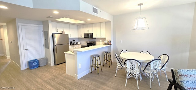 kitchen featuring a breakfast bar area, tasteful backsplash, white cabinetry, kitchen peninsula, and stainless steel appliances