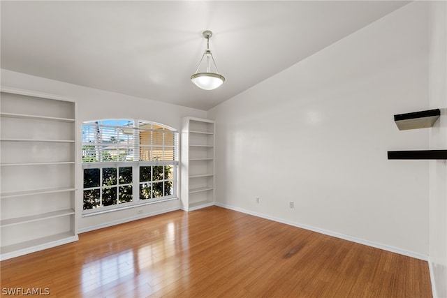 empty room with built in shelves, wood-type flooring, and vaulted ceiling