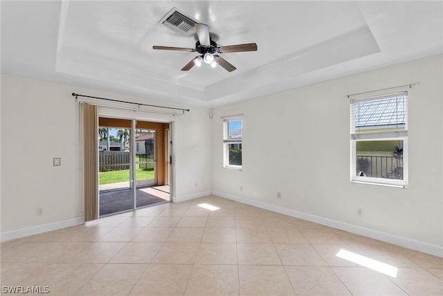 tiled empty room featuring ceiling fan and a raised ceiling