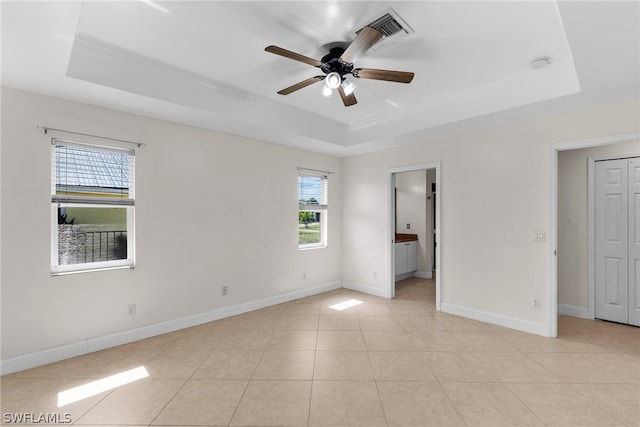 tiled empty room with a raised ceiling and ceiling fan