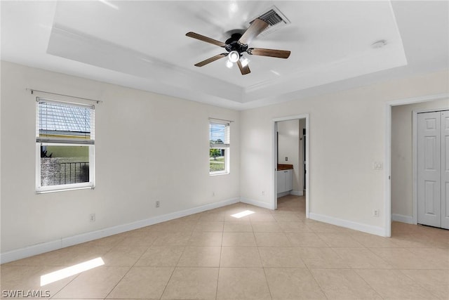 unfurnished bedroom with multiple windows, light tile patterned floors, a tray ceiling, and connected bathroom