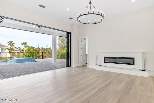 unfurnished living room featuring an inviting chandelier and light hardwood / wood-style flooring