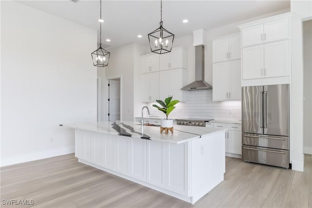 kitchen featuring wall chimney exhaust hood, white cabinetry, a kitchen island with sink, and high end refrigerator