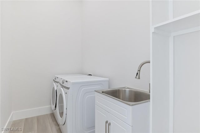 clothes washing area with cabinets, light hardwood / wood-style flooring, washer and clothes dryer, and sink