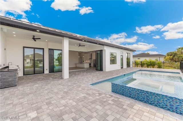 back of house featuring a swimming pool with hot tub, ceiling fan, a patio area, and exterior kitchen