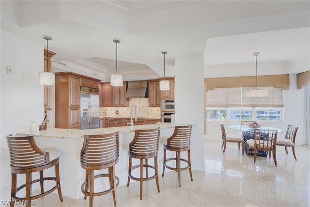 kitchen featuring light stone counters, a tray ceiling, stainless steel appliances, custom exhaust hood, and pendant lighting