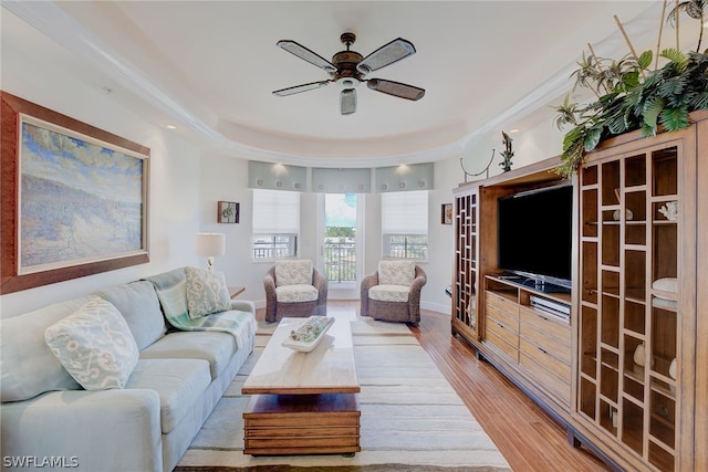 living room with light hardwood / wood-style floors, ceiling fan, and a tray ceiling