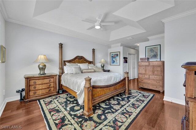 bedroom featuring ceiling fan, dark hardwood / wood-style floors, crown molding, a tray ceiling, and a closet