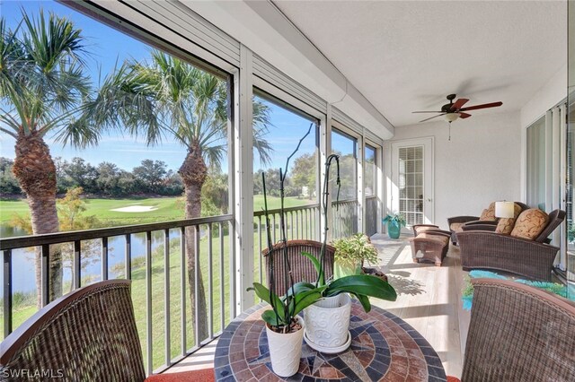 sunroom with ceiling fan and a water view