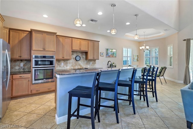 kitchen featuring a breakfast bar, hanging light fixtures, a center island with sink, and a tray ceiling