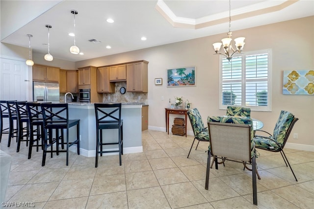 kitchen featuring pendant lighting, decorative backsplash, a tray ceiling, a breakfast bar area, and stainless steel appliances