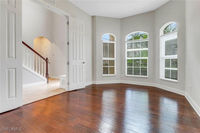 7787 Martino Cir, Naples, FL 34112 - unfurnished room featuring arched walkways, hardwood / wood-style floors, and stairs
