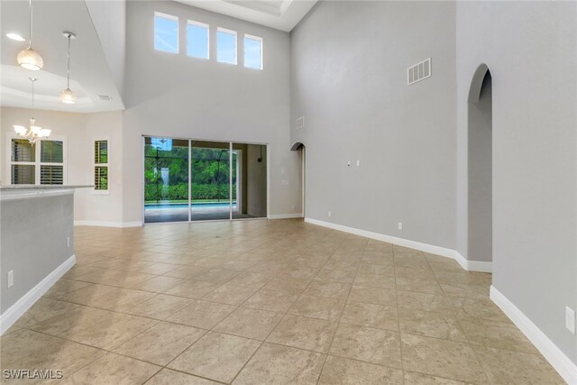 7787 Martino Cir, Naples, FL 34112 - unfurnished living room with a chandelier, healthy amount of natural light, a high ceiling, tile patterned flooring, and arched walkways