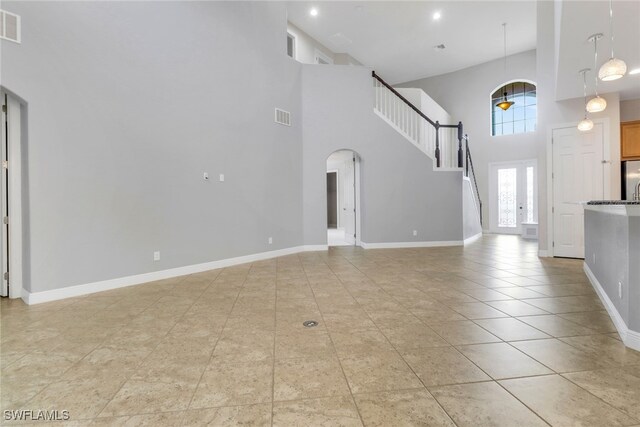 7787 Martino Cir, Naples, FL 34112 - unfurnished living room featuring arched walkways, a towering ceiling, light tile patterned floors, and stairs