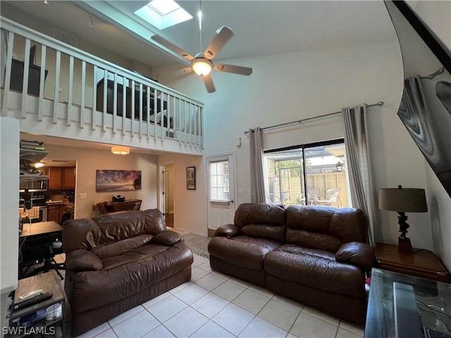 tiled living area with a skylight, ceiling fan, a towering ceiling, and baseboards