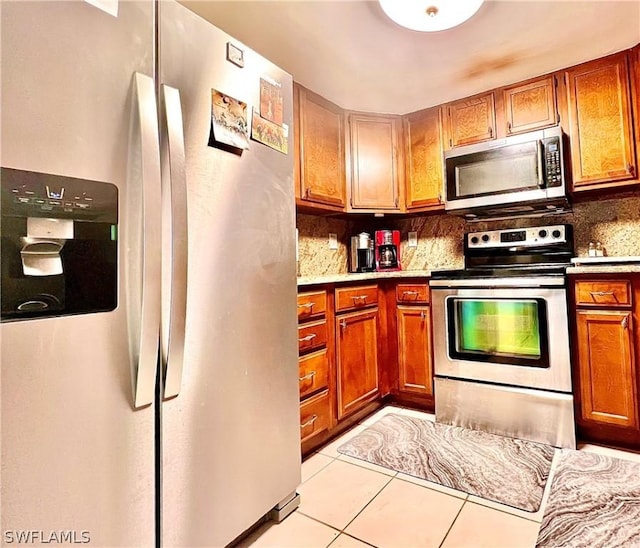 kitchen with light tile patterned flooring, stainless steel appliances, light countertops, brown cabinets, and tasteful backsplash