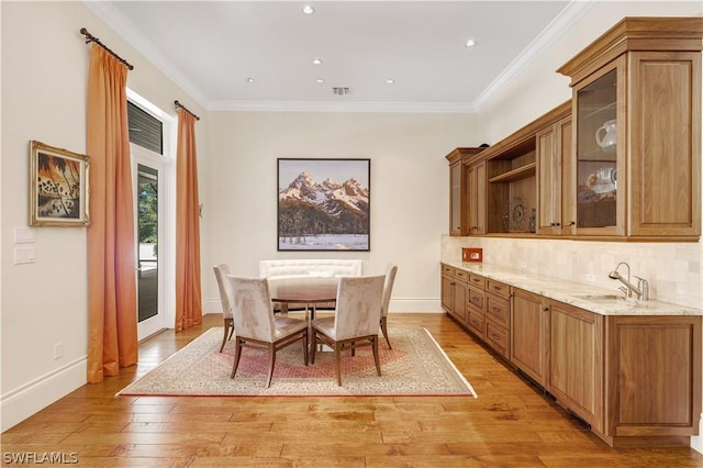 dining room featuring ornamental molding, sink, and light hardwood / wood-style flooring