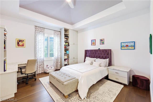 bedroom with dark wood-type flooring, a raised ceiling, and ceiling fan