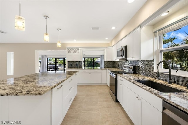 kitchen with a kitchen island, appliances with stainless steel finishes, light stone counters, white cabinetry, and a sink