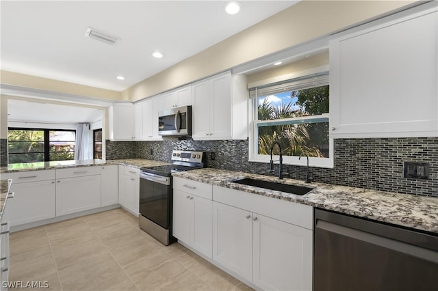 kitchen with stainless steel appliances, light stone counters, a sink, and white cabinets