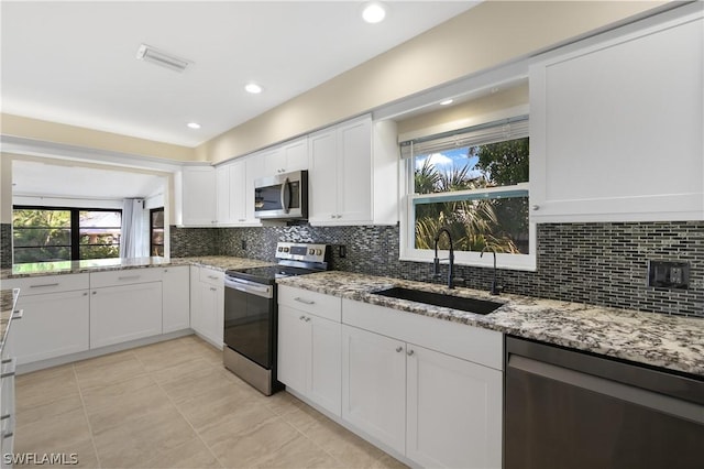 3461 Lakeview Dr, Naples, FL 34112 - kitchen featuring stainless steel appliances, a sink, white cabinetry, decorative backsplash, and light stone countertops