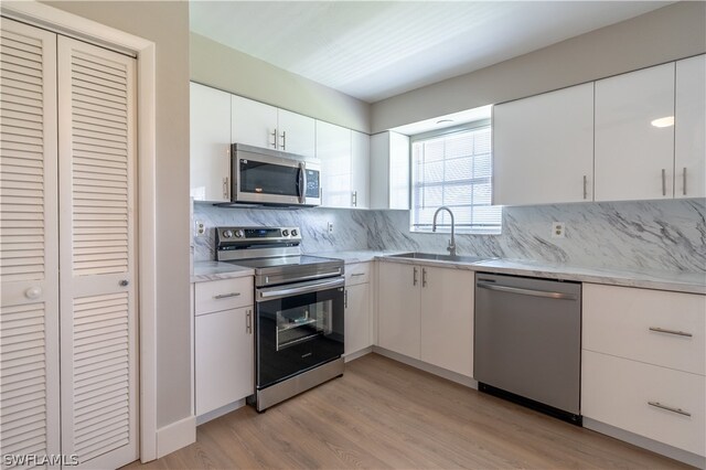 kitchen with light wood-type flooring, white cabinets, appliances with stainless steel finishes, decorative backsplash, and sink