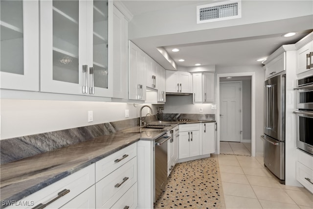 kitchen with appliances with stainless steel finishes, dark stone counters, white cabinets, sink, and light tile patterned flooring