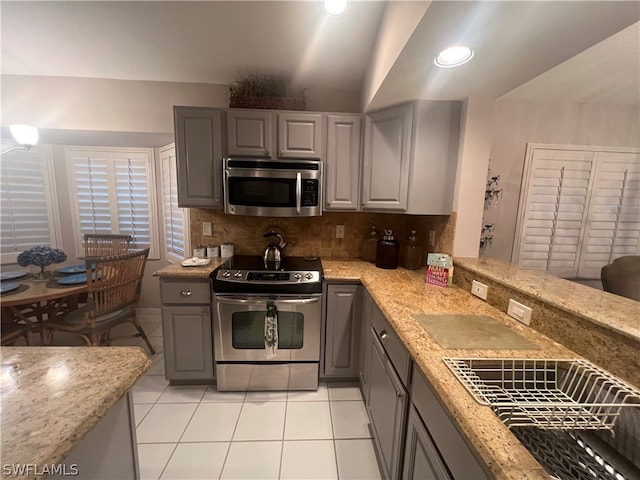 kitchen featuring tasteful backsplash, stainless steel appliances, light stone counters, gray cabinets, and light tile patterned floors