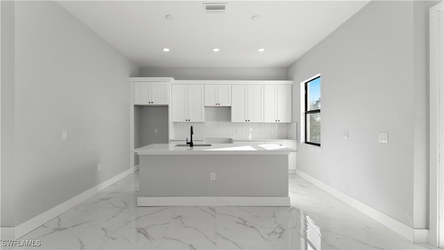 kitchen featuring decorative backsplash, white cabinetry, sink, and an island with sink