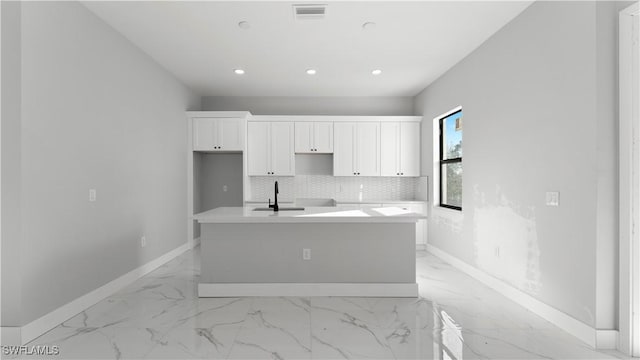 kitchen featuring tasteful backsplash, a kitchen island with sink, sink, and white cabinets