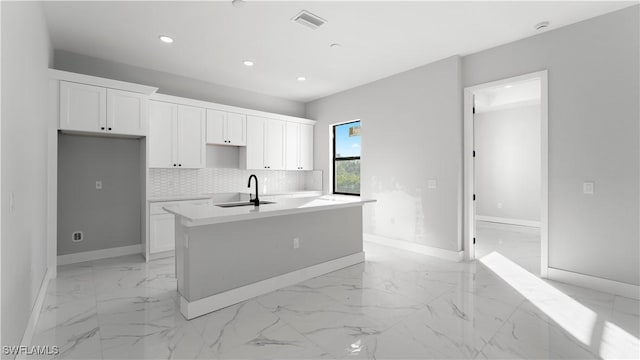 kitchen with a center island with sink, backsplash, white cabinetry, and sink