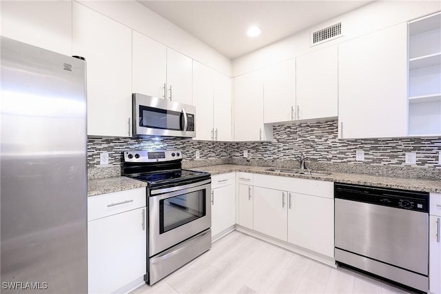 kitchen with sink, white cabinets, stainless steel appliances, light stone countertops, and backsplash