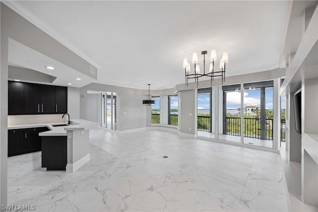 kitchen with an inviting chandelier, a center island with sink, sink, hanging light fixtures, and ornamental molding