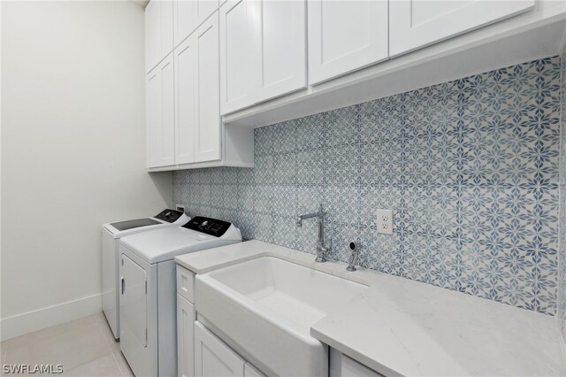 clothes washing area with sink, washing machine and dryer, cabinets, and light tile patterned flooring